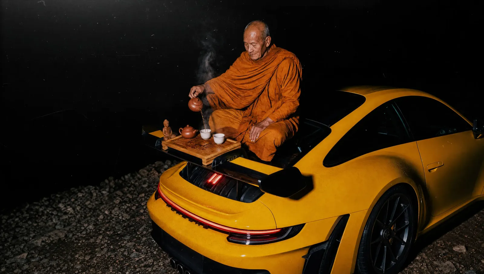 Monk performing a tea ceremony on a yellow sports car